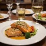 Delicious plating of Friends Phoebe Buffay's Smelly Cat Salmon served with vegetables and wine for a complete dining experience.