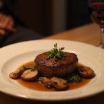 Final presentation of Hannibal Jack Crawford's FBI Filet Mignon mushrooms on a dining table with a glass of red wine in a fine dining setting.