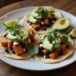 Final presentation of The Euphoria Zendaya's Sweet Potato and Black Bean Tacos garnished with avocado and lime on a rustic table. A tempting and vibrant dish ready to enjoy.