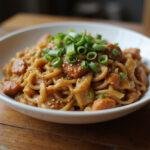 A delicious serving of Uncharted Tom Holland's Adventure Noodle Stir-fry on a rustic wooden table, garnished with green onions and sesame seeds.