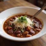 Serving of Wonka's Timothée Chalamet Chocolate Chili with fresh herbs and cheese, a stunning and delicious dish.