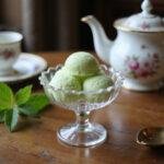 A close-up of Violet, the Dowager Countess, enjoying a scoop of her homemade Verveine sorbet served in an elegant vintage bowl inside the grand drawing room, with period-appropriate furnishings and soft daylight streaming through tall windows, emphasizing the refined atmosphere of Downton Abbey.