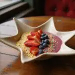 A vibrant star-shaped smoothie bowl topped with fresh fruit, edible gold flakes, and sprinkles on a wooden table with Hollywood-inspired decor, evoking the romantic and dreamy ambiance of La La Land. Perfectly styled as a movie-inspired breakfast scene.