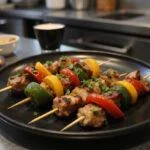 A close-up image of Marvel Elektra's Sai Skewers displayed on a sleek black plate, with vibrant grilled vegetables and perfectly cooked meat pieces. The background features a metallic kitchen countertop with Marvel superhero-themed decorations, highlighting a superhero food presentation inspired by Elektra from Marvel.
