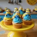Close-up of Kevin King Bob cupcakes decorated with Minions faces and bright yellow frosting, displayed on a yellow cake stand in a cheerful kitchen inspired by the Minions movie, with themed decorations around them.