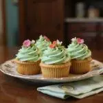 Betty Cooper's Sweet Pea Cupcakes arranged on a vintage plate in a cozy Riverdale kitchen with pastel green frosting and edible flower toppings, with Riverdale-themed decorations in the background.