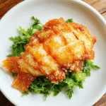 Golden-brown Magikarp-shaped tempura fish with crispy, airy batter, arranged on a white plate with green garnish, vibrant and appetizing.