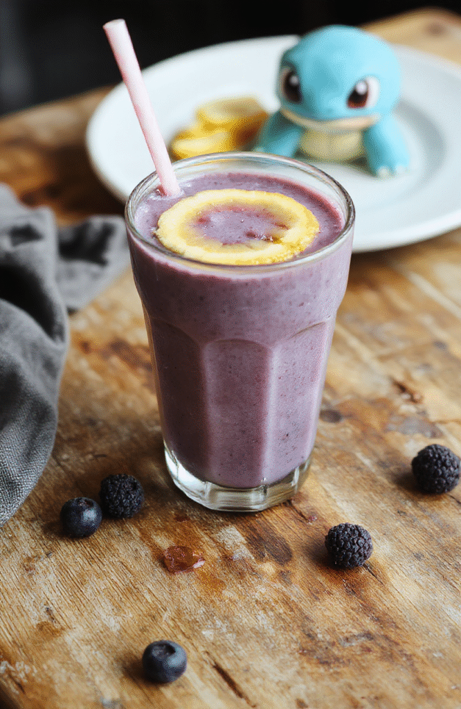 A vibrant blue smoothie with fresh blueberries in a clear glass with a striped straw, garnished with a few blueberries and mint leaves, placed on a wooden rustic table with a soft-focus background of a colorful cartoon-inspired kitchen scene.