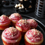 Vibrant cupcakes decorated with galaxy-inspired swirls and cinema-themed toppers, placed on a sleek dark surface with cinematic props in the background, vibrant colors with a glossy finish.