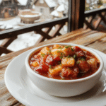 A vibrant bowl of Frozen Arendelle Winter Stew featuring hearty chunks of vegetables and tender meat, topped with fresh herbs. The stew is served in a rustic ceramic bowl on a wooden table, with steam rising, highlighting rich, warm colors and a thick, comforting texture. Snowflake-shaped bread slices and a sprinkle of herbs add to the cozy, magical winter scene.