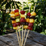 Vibrant fruit skewers arranged on a rustic wooden platter, featuring colorful strawberries, pineapple chunks, green grapes, and melon slices. The skewers are neatly aligned, showcasing the fresh, juicy textures, with a backdrop inspired by the lush greenery of Middle-earth, styled to evoke a magical, fantasy atmosphere.