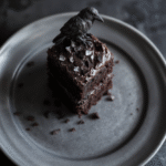 A striking black velvet cake with smooth, velvety frosting decorated with edible silver pearls and dark purple accents, plated on a black matte surface with a mystical, Gothic ambiance.