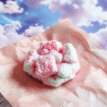 A vibrant, whimsical sky-colored cotton candy resembling clouds on a clear blue plate, topped with edible glitter to mimic sparkling sky, set against a soft pastel background with fantasy-themed decorations.