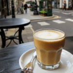 A steaming London Fog Latte in a clear glass mug with a delicate layer of frothy milk on top, infused with a hint of vanilla and Earl Grey tea, styled with a lemon twist on the rim. The drink sits on a vintage wooden table with soft ambient lighting, highlighting its creamy texture and tea-infused aroma, evoking a cozy Victorian ambiance.