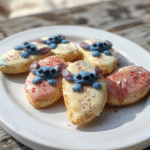 Colorful Stitch surfboard shaped sugar cookies decorated with vibrant icing, sprinkles, and themed toppings, arranged on a rustic white platter with a beachy backdrop, capturing the playful and cinematic vibe.