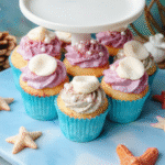 Colorful Ariel's seashell cupcakes arranged on a nautical-themed tray. The cupcakes feature shimmering pastel pink, purple, and blue frosting with edible pearl accents resembling seashells, set against a vibrant ocean-inspired backdrop with hints of glitter and coral decorations.
