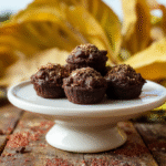 Three small mason jar-style cups filled with chocolate cookie crumble 'dirt,' vibrant green avocado mousse 'grass,' and playful gummy insects (worms and beetles) on top, with dew drops and edible flower petals for detail, placed on a rustic wooden table.