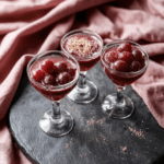 A shimmering glass filled with vibrant purple grape mocktail dotted with edible glitter, garnished with fresh grapes and mint leaves, placed on a dark marble surface with soft golden lighting, evoking the stylish and dramatic aesthetic of the TV show Euphoria.