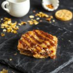 A decadent, glossy Traitors toffee pudding served in a dark ceramic ramekin, rich golden-brown toffee sauce draining down the sides, topped with a quenelle of vanilla bean ice cream and a shard of brittle toffee, garnished with edible gold dust and.cracked sea salt, on a rustic wooden board with subtle steam rising