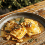 Plump, golden-brown mushroom ravioli arranged in a elegant swirl on a rustic wooden board, garnished with fresh sage leaves, crushed pistachios, and a drizzle of golden brown butter. Background features soft twilight lighting with subtle fog and distant gothic trees, evoking a mystical forest ambiance.