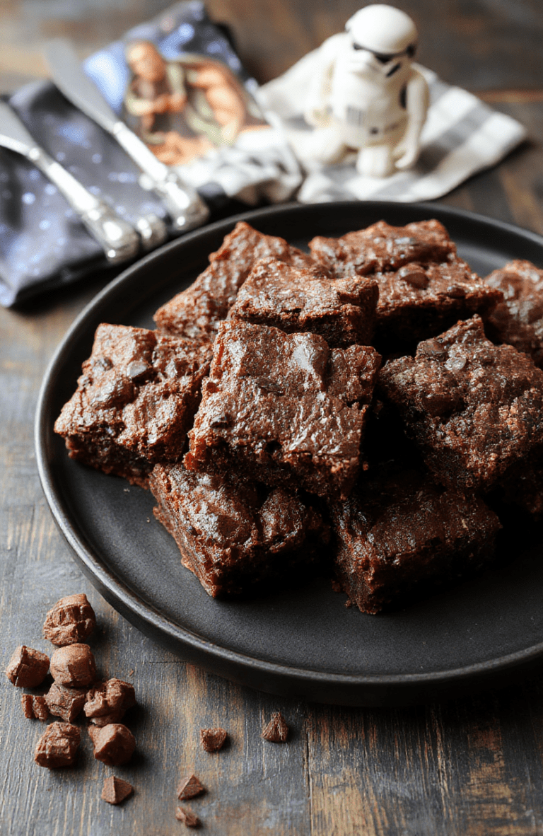 Close-up of glossy fudgy brownies cut into squares on a dark slate plate, with a light cocoa dusting and toasted coconut to resemble Chewbacca fur, set against a starry backdrop that nods to a galaxy far, far away.